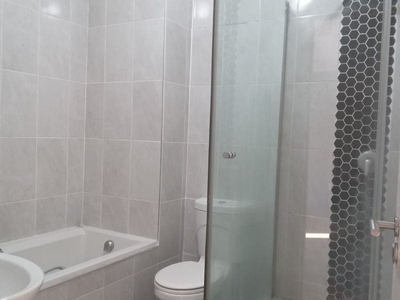 A modern bathroom featuring a built-in bathtub, a separate glass-enclosed shower with mosaic accent tiling, a toilet, and a washbasin.