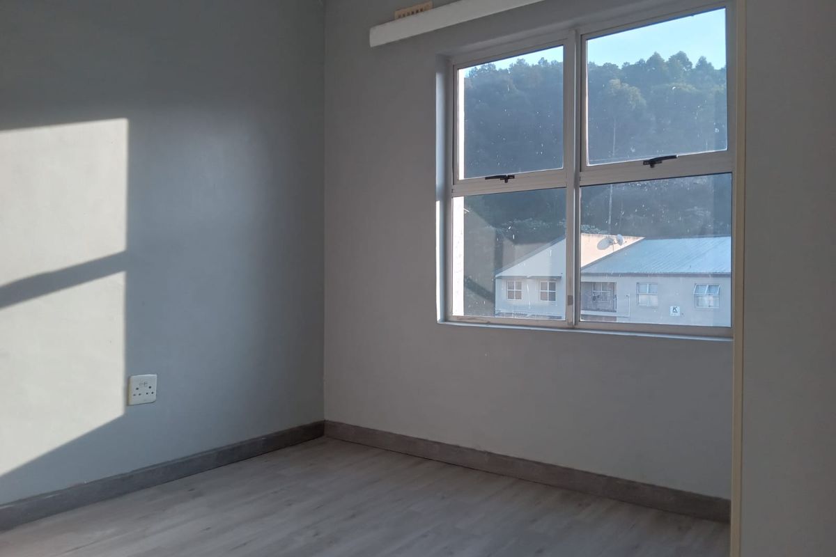 A vacant bedroom featuring light-toned laminate flooring, grey painted walls, and an aluminium-framed window with natural light.