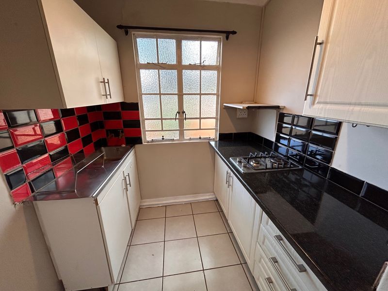 Compact kitchen featuring granite countertops, a gas hob, tiled splashbacks, and built-in cabinetry with tiled flooring.