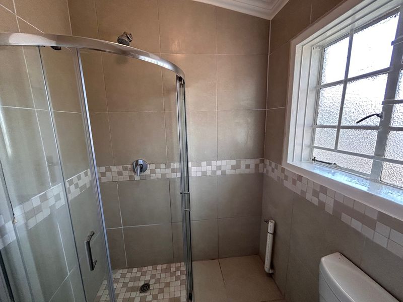 A functional bathroom featuring a glass shower enclosure, tiled walls with decorative accents, and a window with security bars.