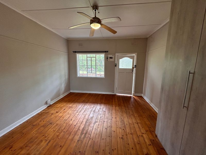 A bright, empty bedroom featuring polished timber flooring, a ceiling fan, and a built-in wardrobe, offering a clean and versatile living space.