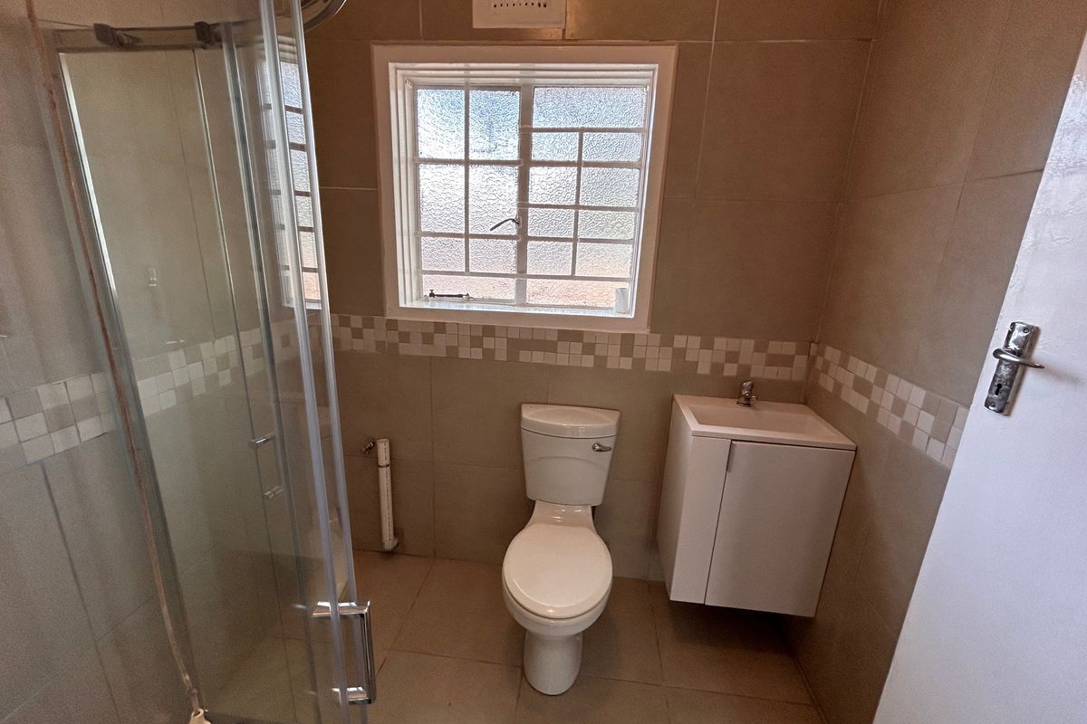 A functional bathroom featuring a glass shower enclosure, wall-mounted vanity, and neutral tiled finishes throughout.