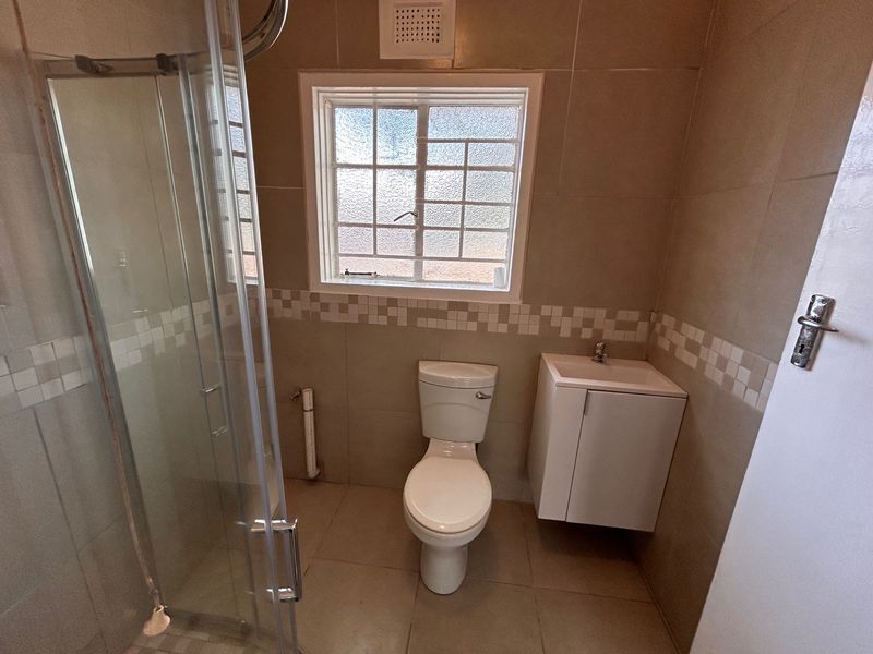 A functional bathroom featuring a glass shower enclosure, wall-mounted vanity, and neutral tiled finishes throughout.