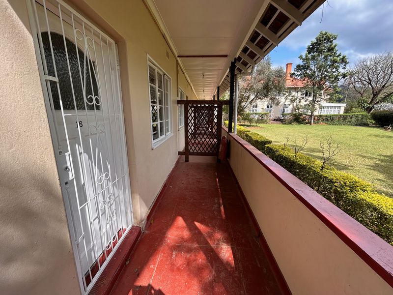 A covered outdoor balcony featuring a security gate, lattice privacy screen, and views over the communal garden area.