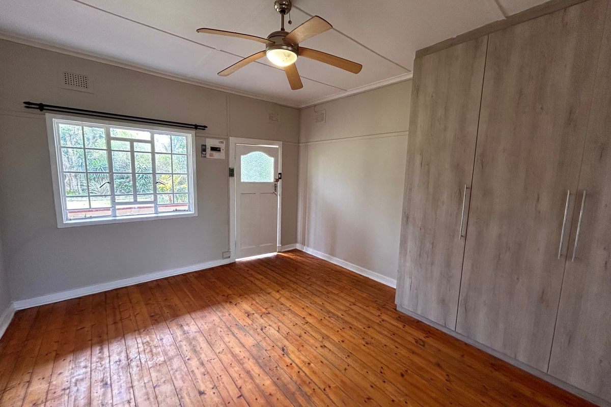 Spacious bedroom featuring polished timber flooring, built-in cupboards, and a ceiling fan, offering a clean and functional living space.