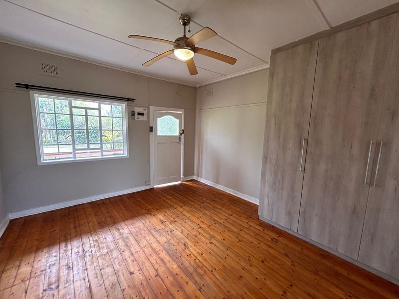 Spacious bedroom featuring polished timber flooring, built-in cupboards, and a ceiling fan, offering a clean and functional living space.