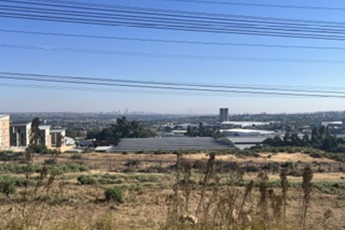 A wide-angle view overlooking a suburban landscape with industrial buildings and distant city skyline, featuring prominent overhead power lines.