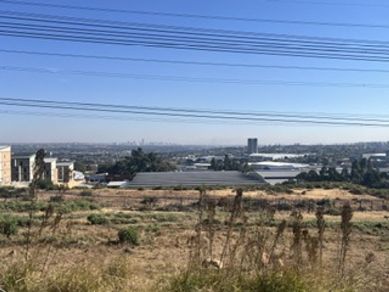 A wide-angle view overlooking a suburban landscape with industrial buildings and distant city skyline, featuring prominent overhead power lines.