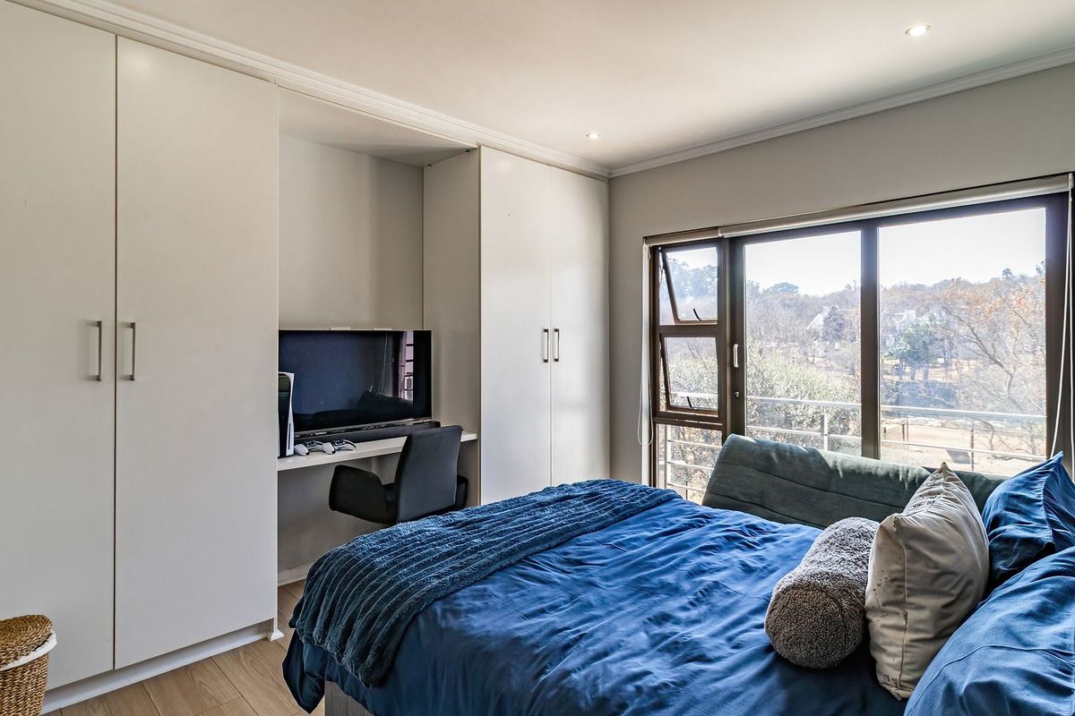 A well-maintained bedroom featuring built-in cupboards, an integrated desk space, laminate flooring, and large windows offering natural light and scenic views.