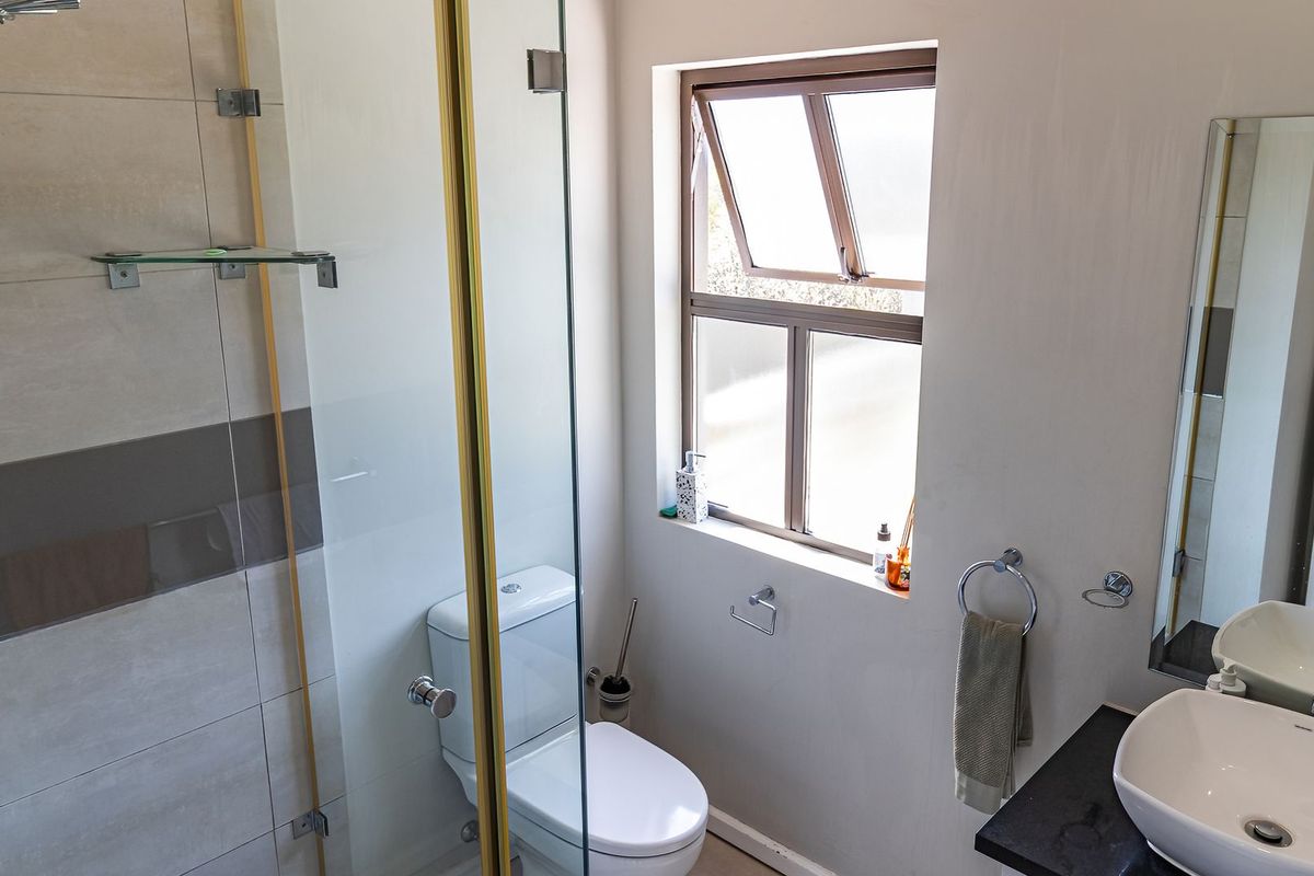A modern, well-maintained bathroom featuring a glass-enclosed shower, a sleek vessel sink on a granite vanity, and neutral wall tiling.