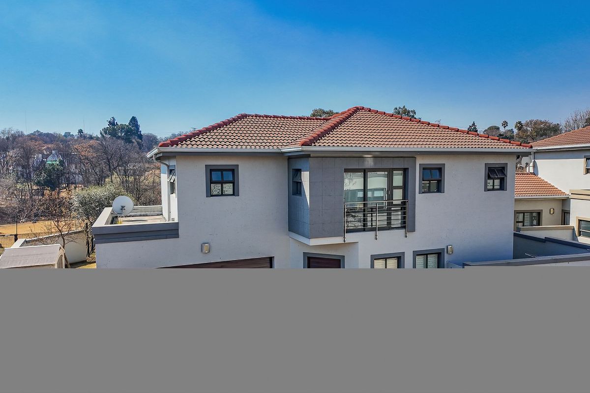 Rear elevation of a modern two-story house featuring a tiled roof, balcony with metal railing, and casement windows.
