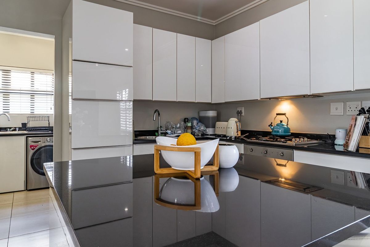 Modern kitchen featuring high-gloss white cabinetry, sleek black granite countertops, a central island, and integrated stainless steel appliances.
