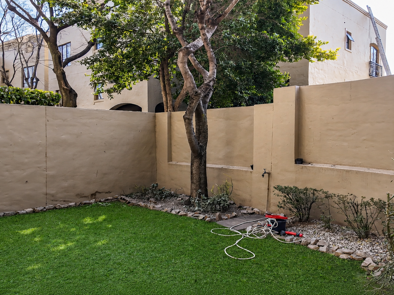 A private rear garden area featuring a well-maintained lawn, boundary walls, and established trees, providing a quiet outdoor space.