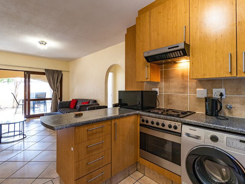 Open-plan kitchen featuring wooden cabinetry, granite countertops, and integrated appliances, flowing into a living area with direct access to a patio through sliding doors.