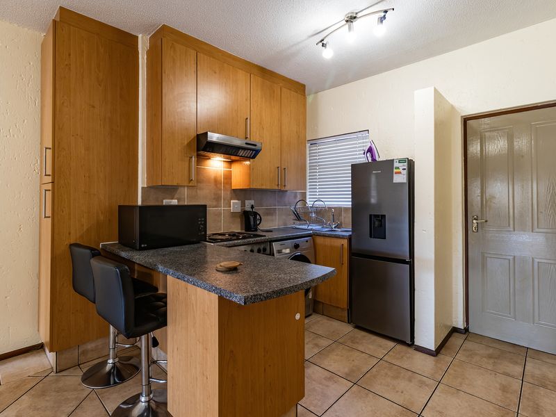 Compact kitchen featuring wood-finish cabinetry, granite countertops, a breakfast bar, and tiled flooring, providing a functional and efficient cooking space.