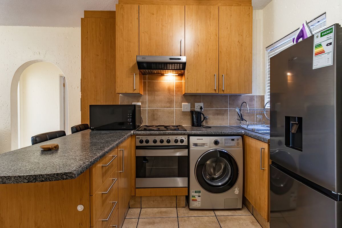 Compact kitchen featuring wooden cabinetry, granite countertops, tiled backsplash, and integrated appliances including an oven, hob, and extractor fan.