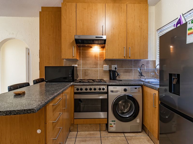 Compact kitchen featuring wooden cabinetry, granite countertops, tiled backsplash, and integrated appliances including an oven, hob, and extractor fan.