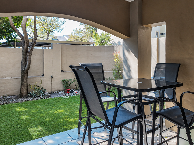 A covered patio area featuring tiled flooring and an arched opening, overlooking a private garden with a perimeter boundary wall.