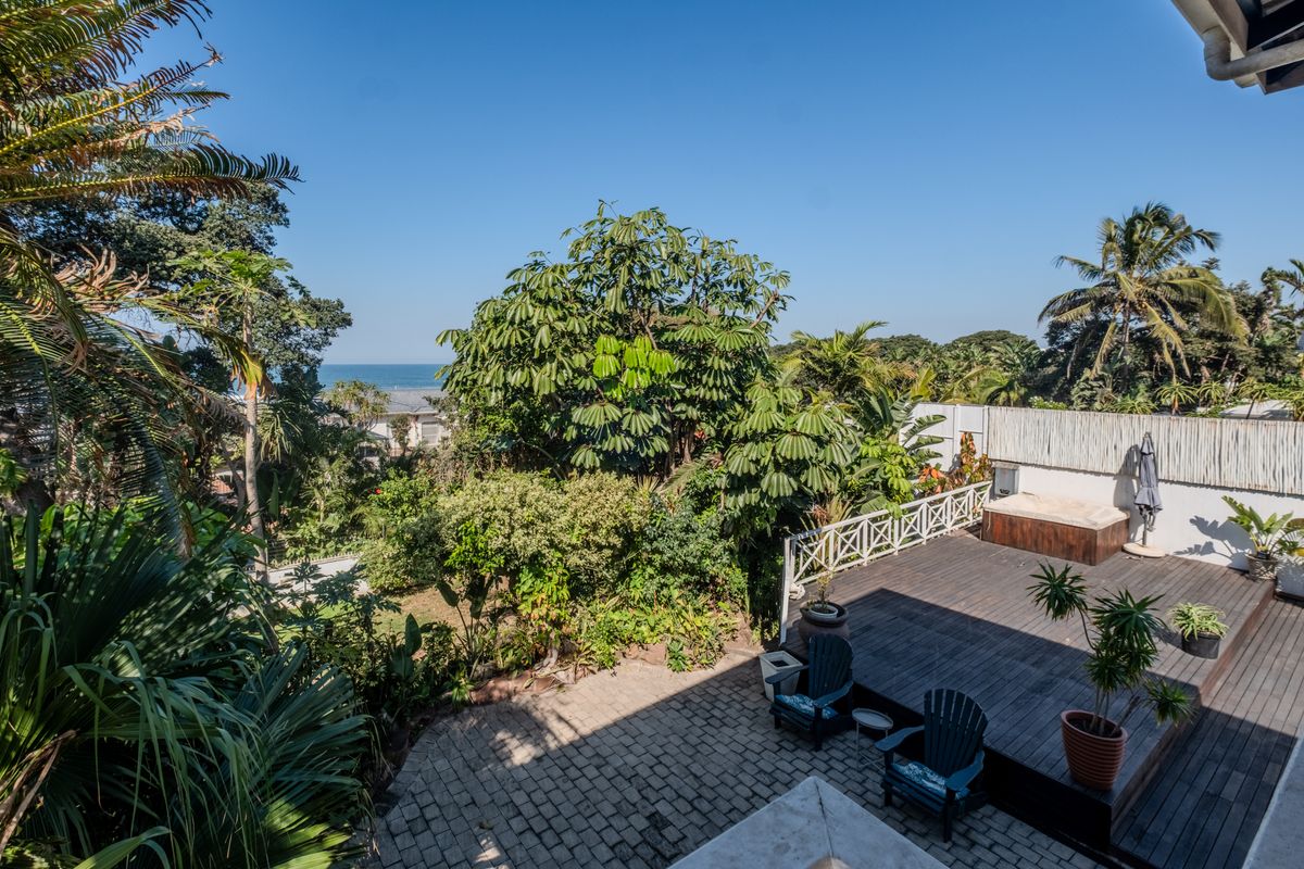Rear outdoor area featuring a timber deck with a built-in hot tub, paved patio space, and lush garden surroundings with distant ocean views.