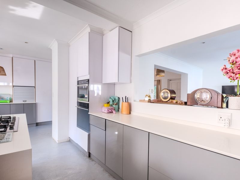 Modern kitchen featuring high-gloss cabinetry, stone countertops, built-in oven, and a convenient pass-through window connecting to the adjacent living area.