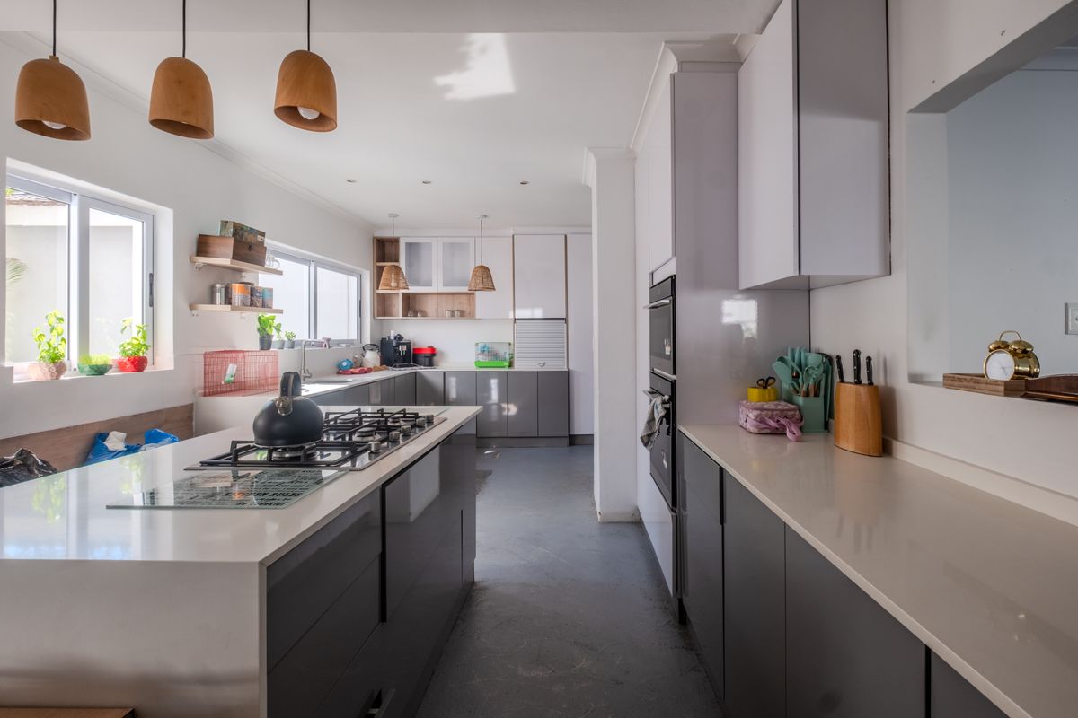 Modern kitchen featuring a central island with a gas hob, sleek grey cabinetry, quartz countertops, and integrated appliances in a bright, open layout.