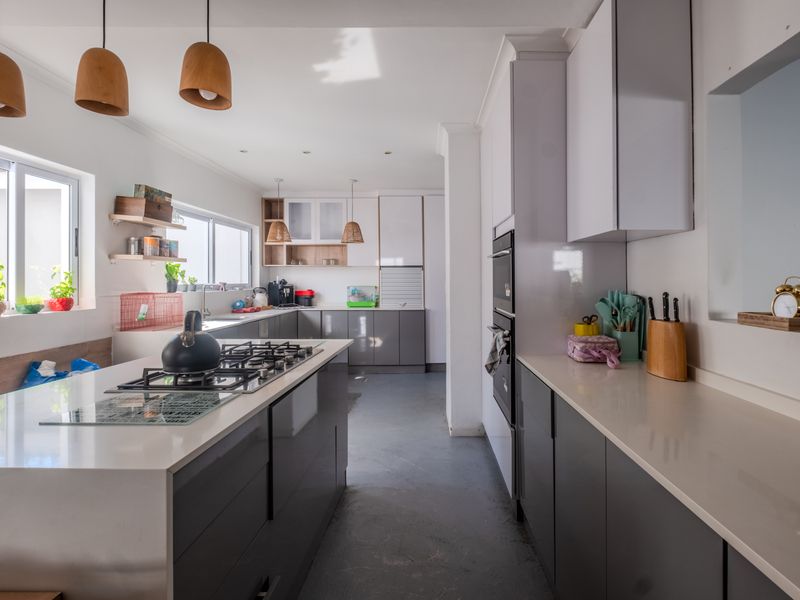 Modern kitchen featuring a central island with a gas hob, sleek grey cabinetry, quartz countertops, and integrated appliances in a bright, open layout.