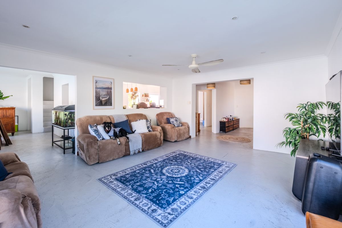 Spacious living room featuring neutral walls, polished concrete flooring, a ceiling fan, and a convenient pass-through window connecting to the adjacent space.
