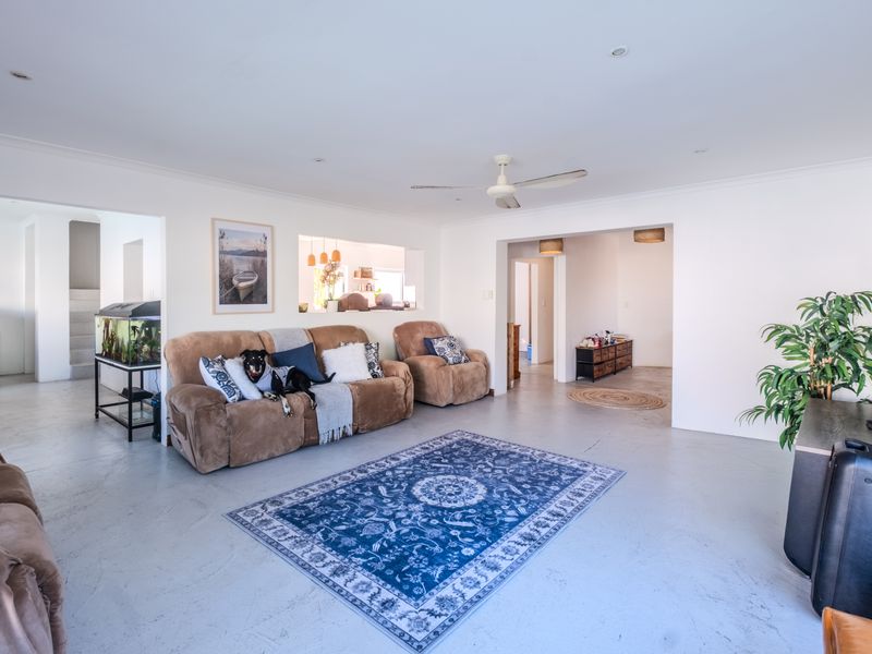 Spacious living room featuring neutral walls, polished concrete flooring, a ceiling fan, and a convenient pass-through window connecting to the adjacent space.