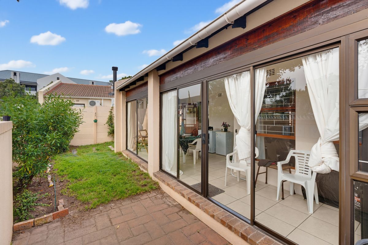 Rear exterior view featuring a paved patio area, sliding glass doors leading to the interior, and a small garden with a brick boundary wall.