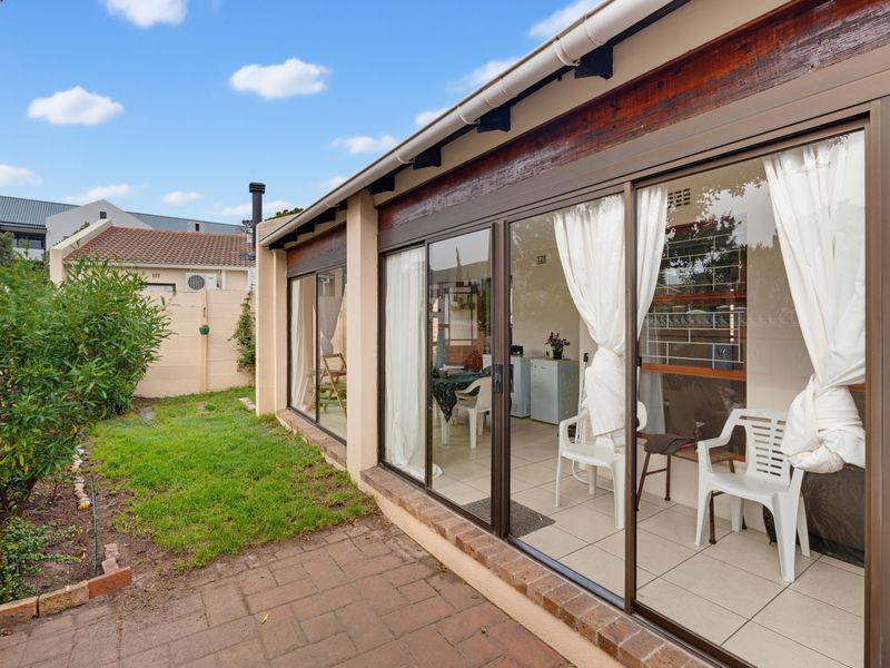 Rear exterior view featuring a paved patio area, sliding glass doors leading to the interior, and a small garden with a brick boundary wall.
