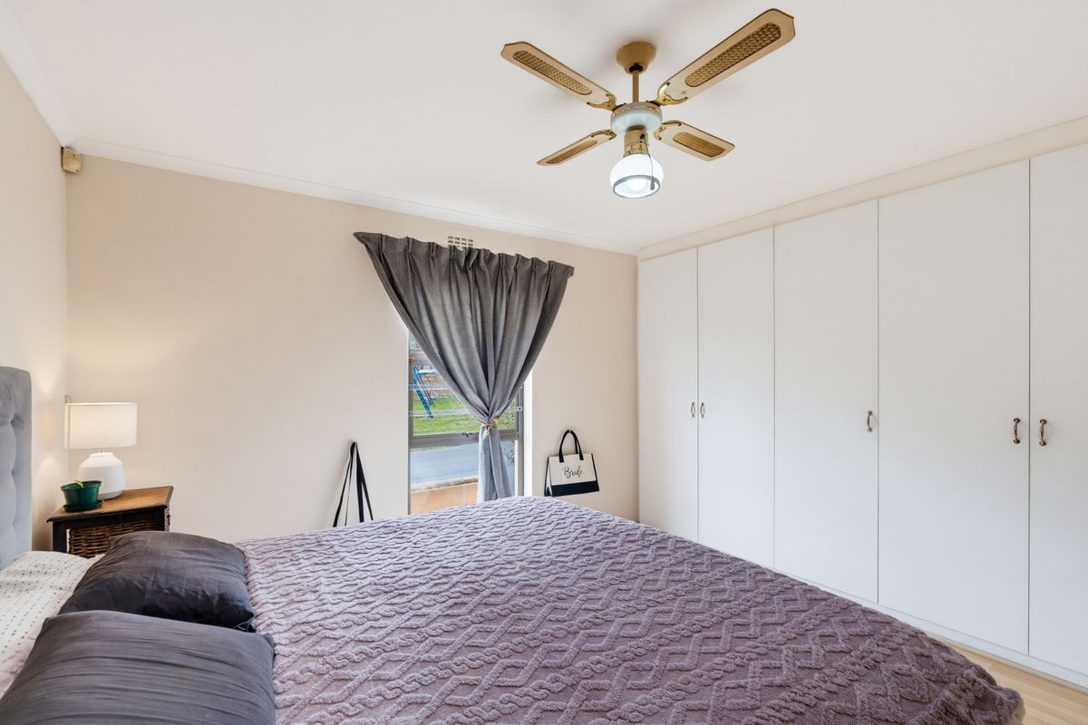 A well-lit bedroom featuring built-in wardrobes, a ceiling fan, and a window with natural light.