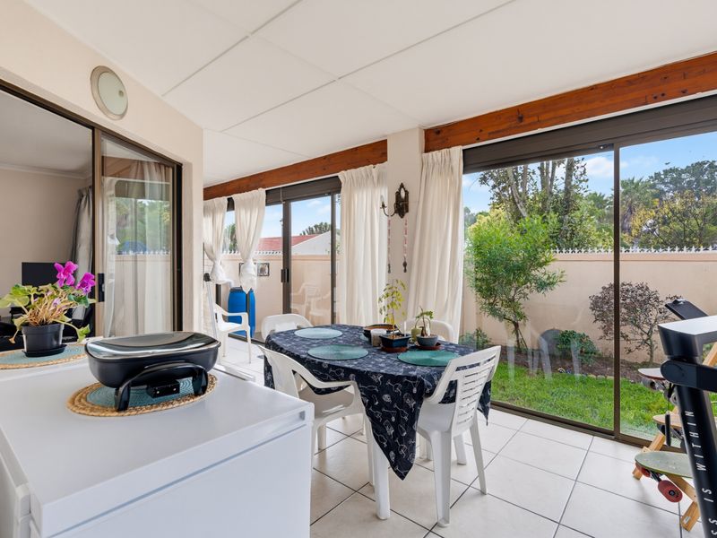 A bright, enclosed patio area featuring tiled flooring, exposed timber beams, and large sliding glass doors providing direct access to the rear garden.