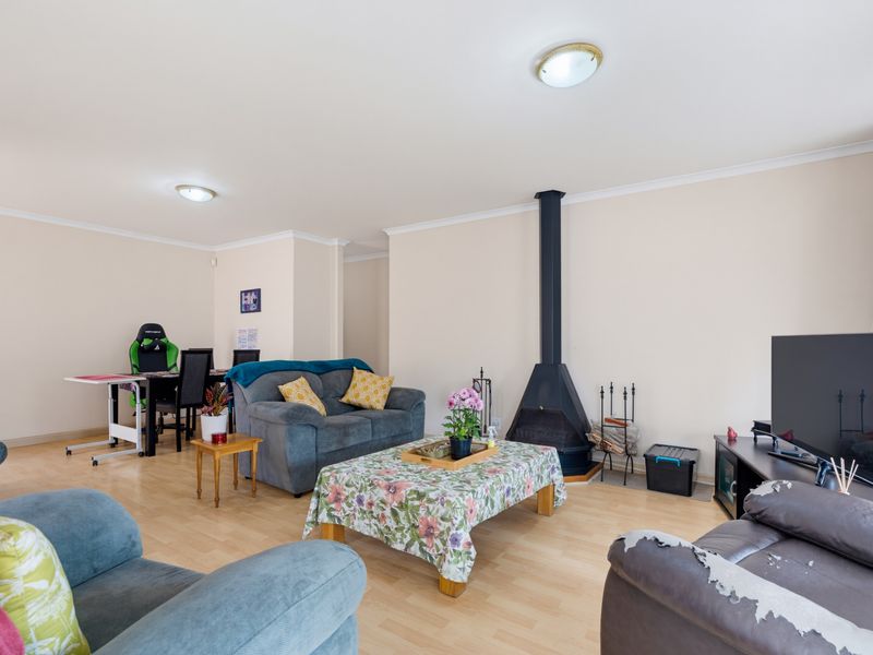 A spacious living room featuring laminate flooring and a central freestanding fireplace, offering a comfortable and functional layout for family relaxation.