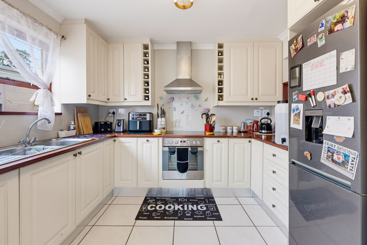A functional U-shaped kitchen featuring cream cabinetry, wooden countertops, stainless steel appliances, and tiled flooring.