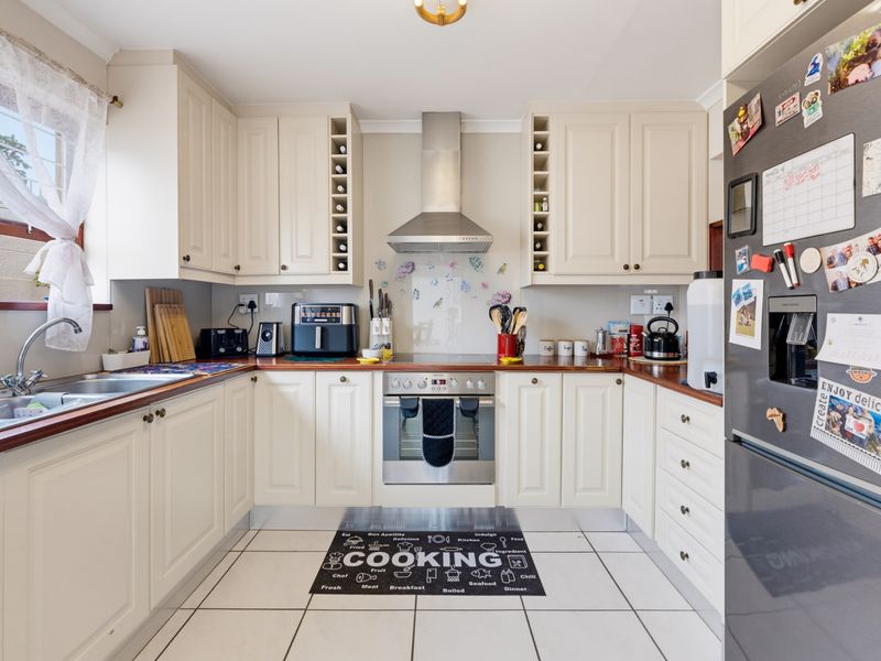 A functional U-shaped kitchen featuring cream cabinetry, wooden countertops, stainless steel appliances, and tiled flooring.