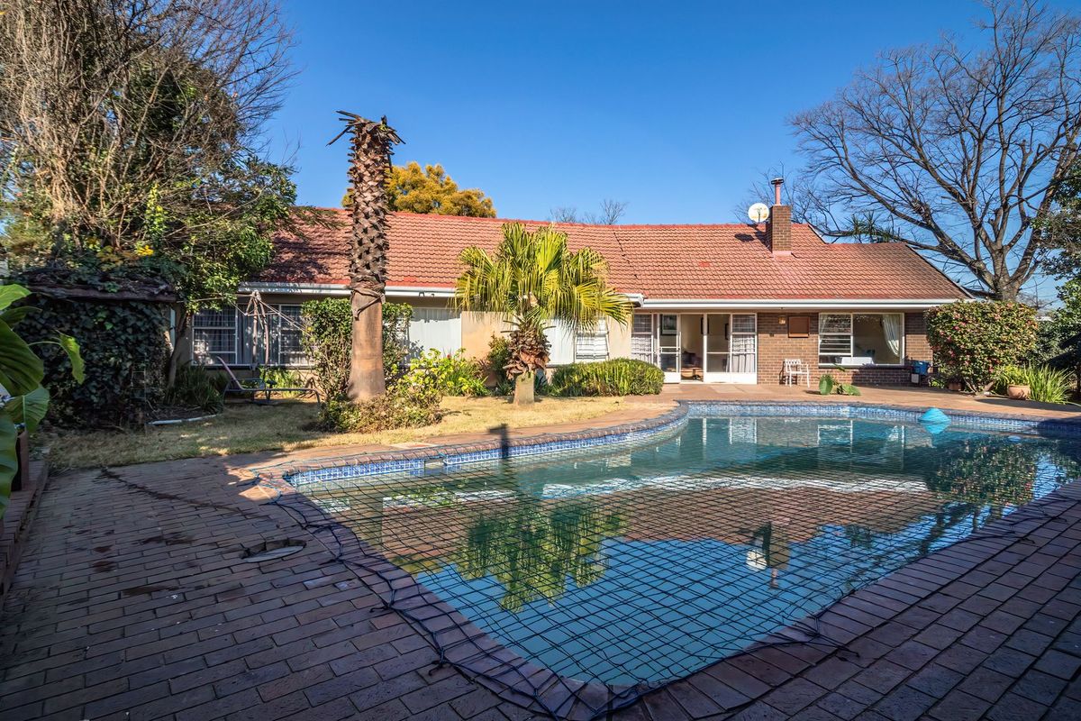 Rear view of the property featuring a swimming pool with safety net, brick paved patio area, and a tiled roof house exterior.