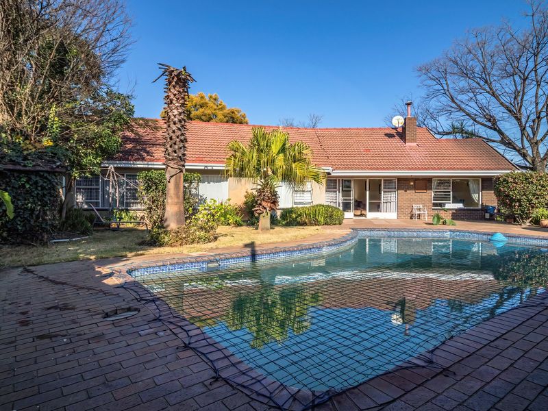 Rear view of the property featuring a swimming pool with safety net, brick paved patio area, and a tiled roof house exterior.