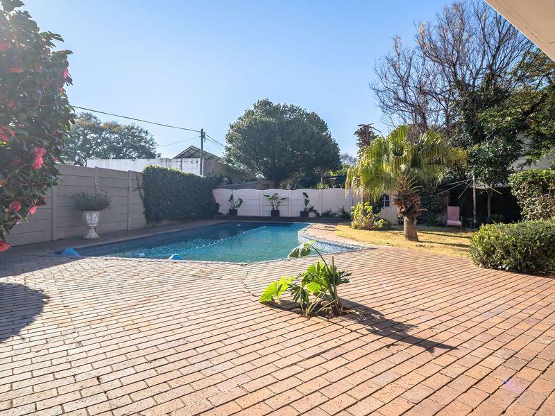 Outdoor pool area featuring a swimming pool, brick paved patio, and established garden surroundings, ideal for outdoor relaxation and entertainment.