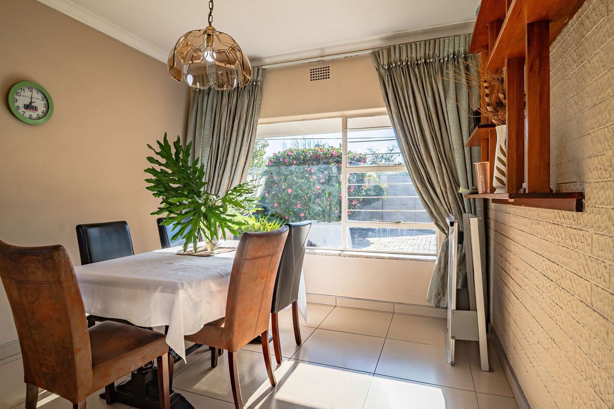 A bright dining room featuring tiled flooring, a large window with natural light, and a textured brick feature wall with built-in shelving.