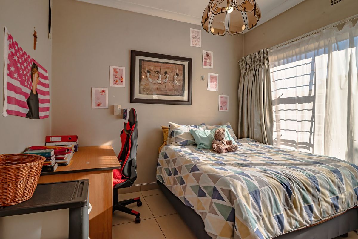 A functional bedroom featuring tiled flooring, neutral wall tones, and natural light through a window with curtain tracks.