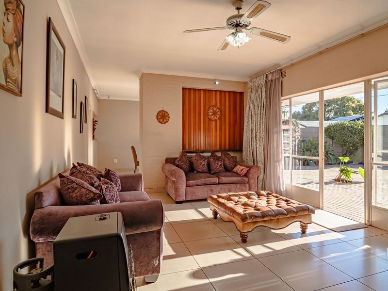 A spacious living room featuring tiled flooring, a ceiling fan, and large sliding glass doors that provide direct access to the outdoor patio area.