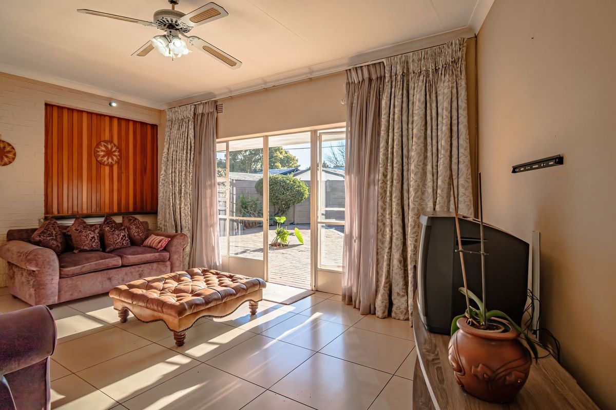 A living room featuring tiled flooring, timber wall paneling, a ceiling fan, and sliding glass doors providing access to the rear patio.