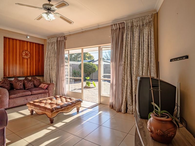 A living room featuring tiled flooring, timber wall paneling, a ceiling fan, and sliding glass doors providing access to the rear patio.