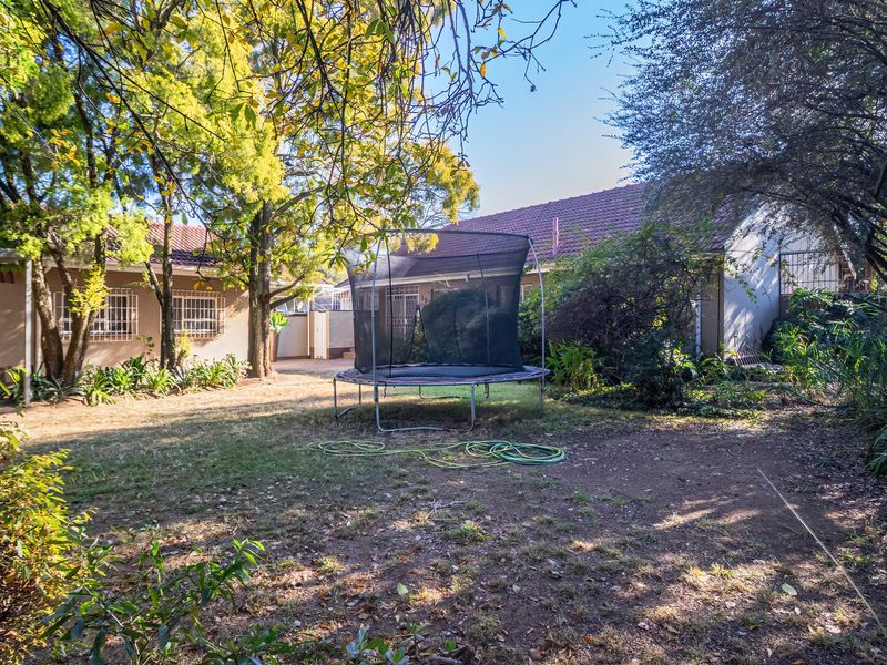 A spacious rear garden area featuring mature trees, a lawn, and a carport, providing a private outdoor space for the property.