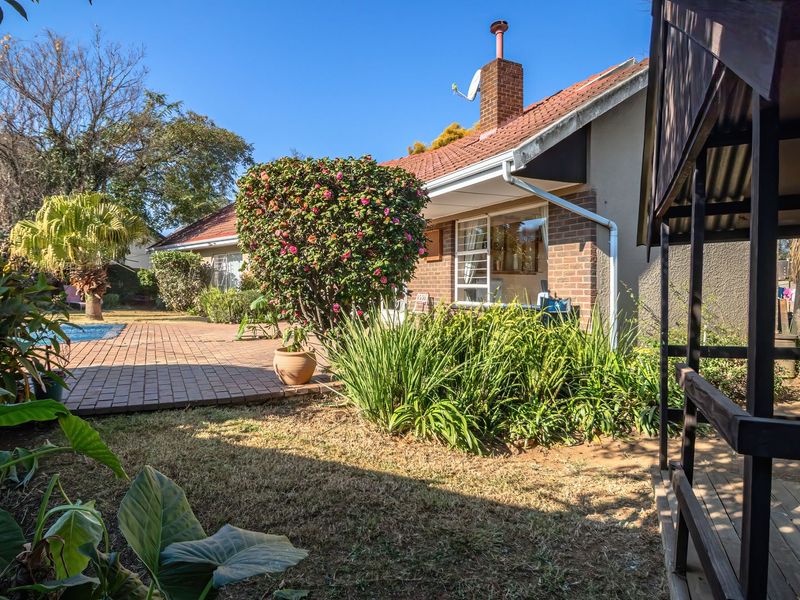 Rear view of the property featuring a brick facade, tiled roof, paved patio area, and a swimming pool set within a landscaped garden.