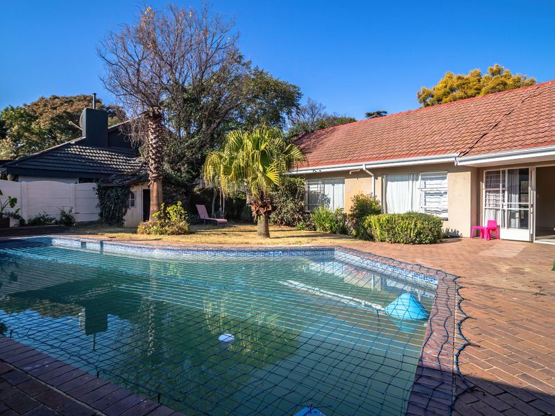 Outdoor pool area featuring a swimming pool with safety net, brick paved patio, and established garden surroundings.