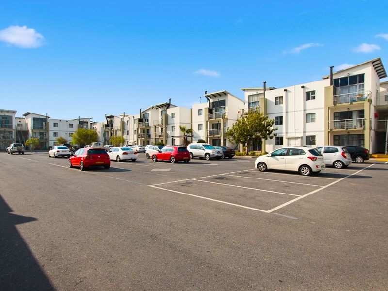 Exterior view of a multi-story apartment complex featuring a paved parking area and modern building facades with balconies and external staircases.