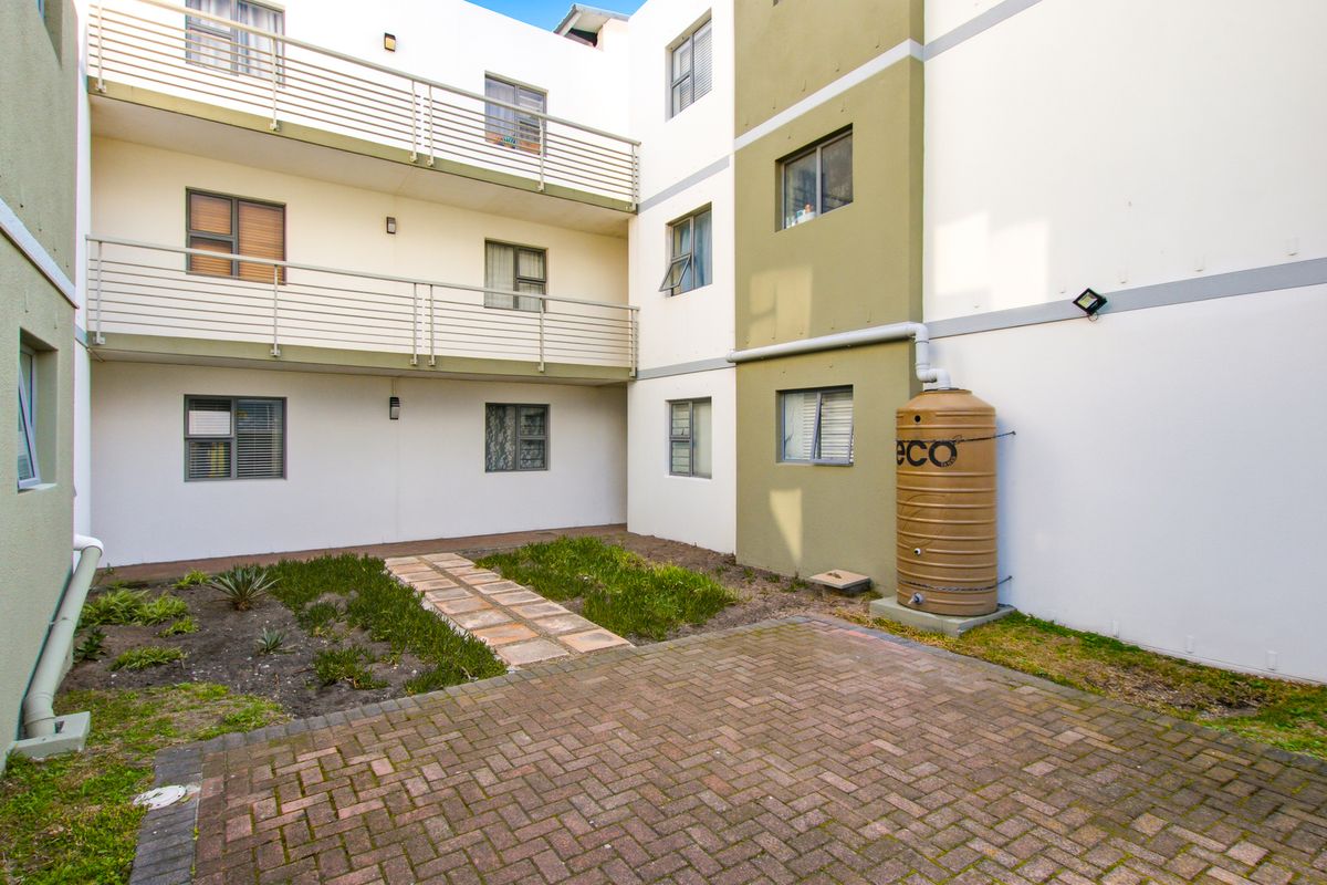 Rear courtyard area of the apartment complex featuring paved surfaces, a small garden patch, and multi-level balconies with metal railings.
