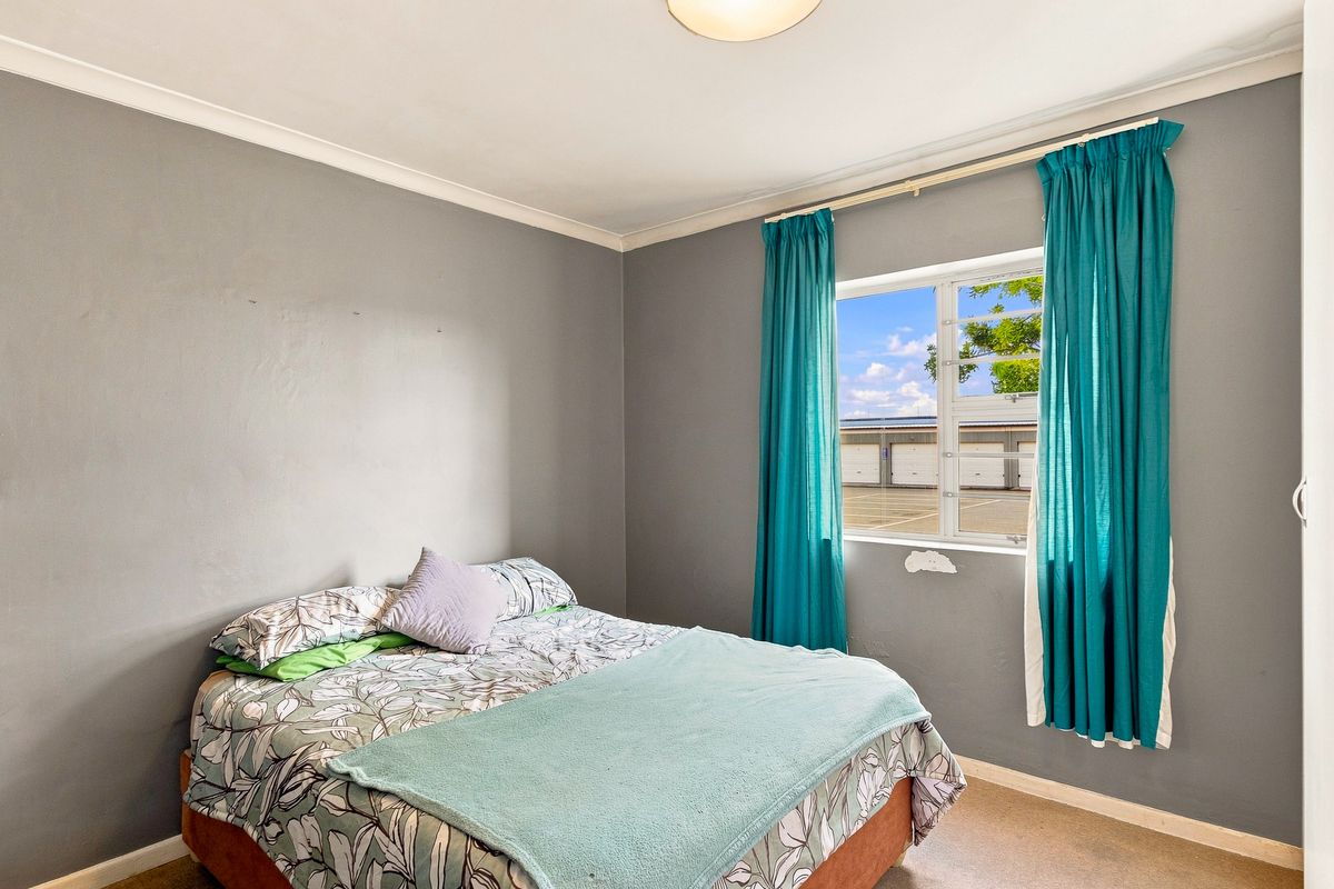 A standard bedroom featuring grey walls, a window with curtain tracks, and coving. The room requires minor repairs to the plasterwork beneath the window.