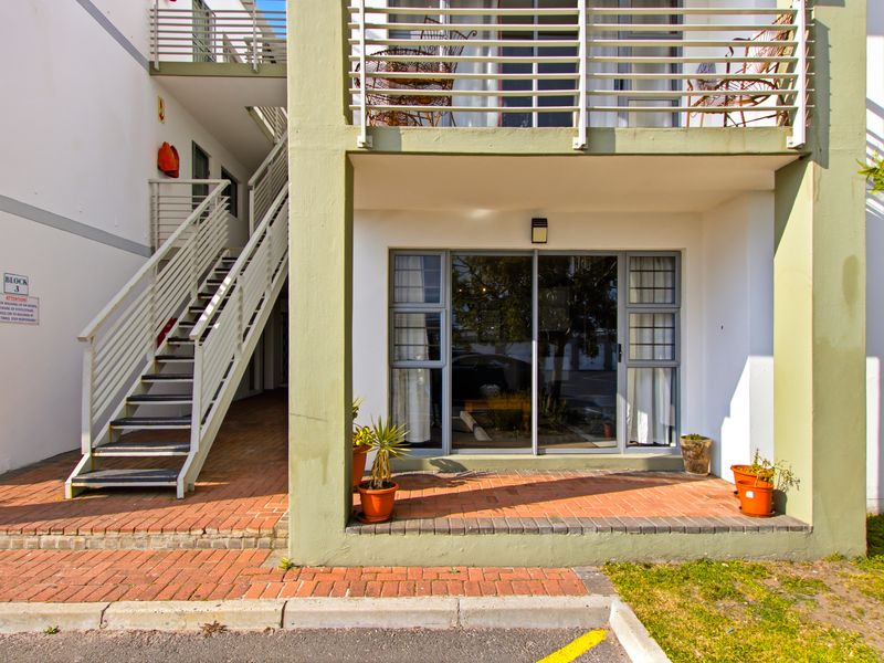Ground floor apartment entrance featuring a brick paved patio, sliding glass doors, and an external metal staircase leading to upper levels.